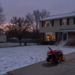A portable generator operating outdoors on a driveway, well away from a snow-dusted home at dusk, illustrating winter weather safety