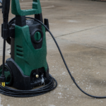 A green and black electric pressure washer on wet concrete outdoors, illustrating the CPSC shock and electrocution warning